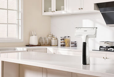Handheld electric mixer resting on a white kitchen island, with white cabinets and a window letting in natural light.